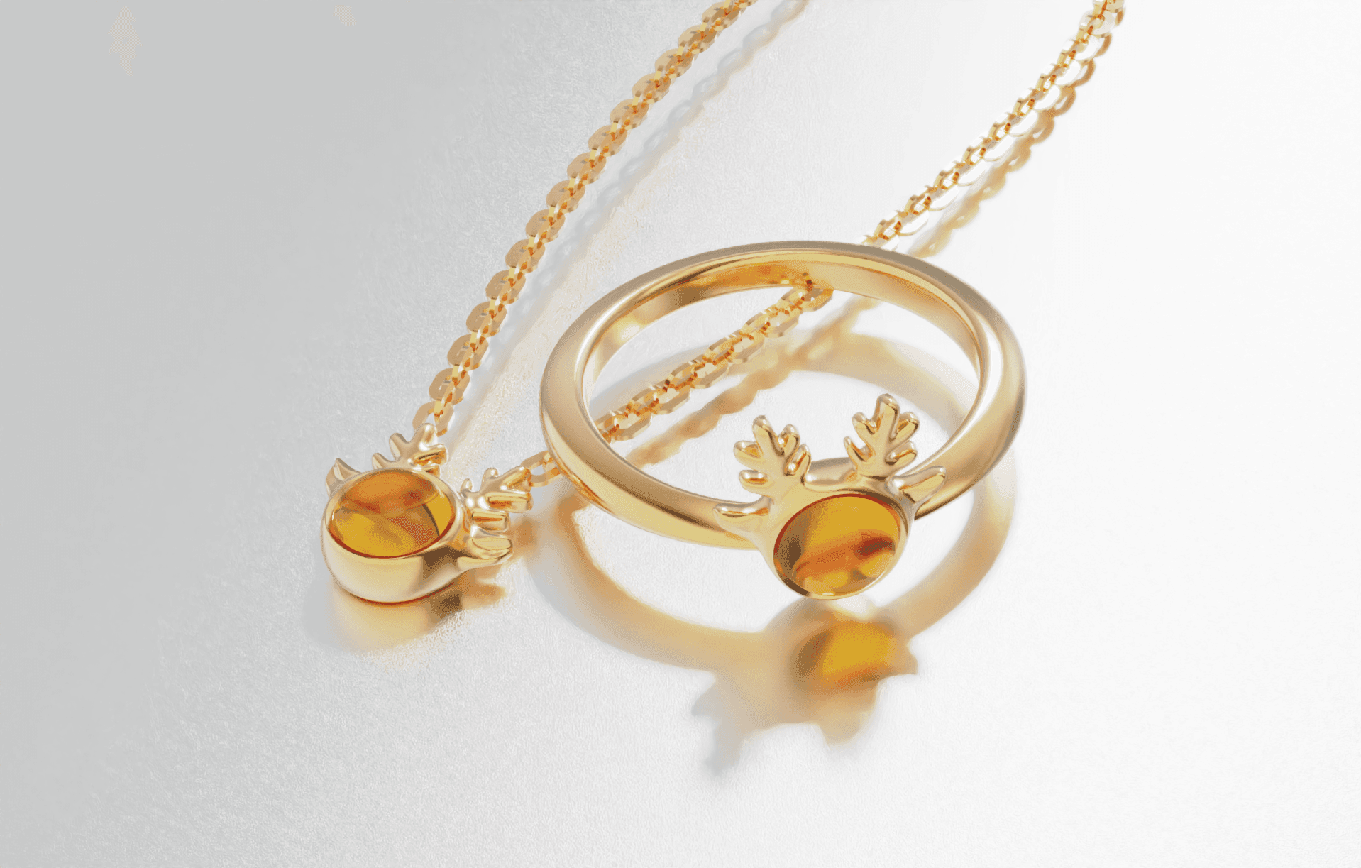 Gold ring and necklace with antler design and amber stones on a reflective surface.